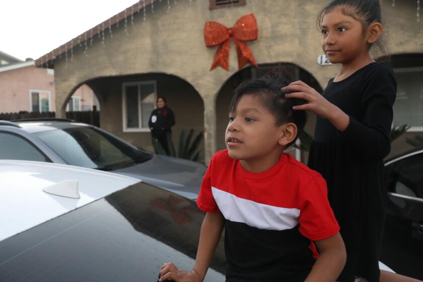 Boyle Heights, CA - December 13: Matthew Rodriguez, 3, left, and Alison Rodriguez, 7, right, play on top of a car as their mom Perla Ortega looks in the background on Wednesday, Dec. 13, 2023 in Boyle Heights, CA. (Michael Blackshire / Los Angeles Times)