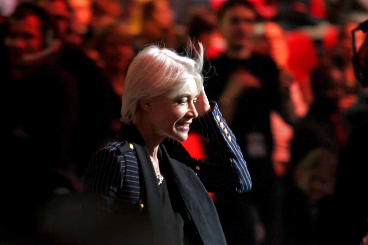 Françoise Hardy, in a black suit jacket and black scarf, smiling as people in the background clap