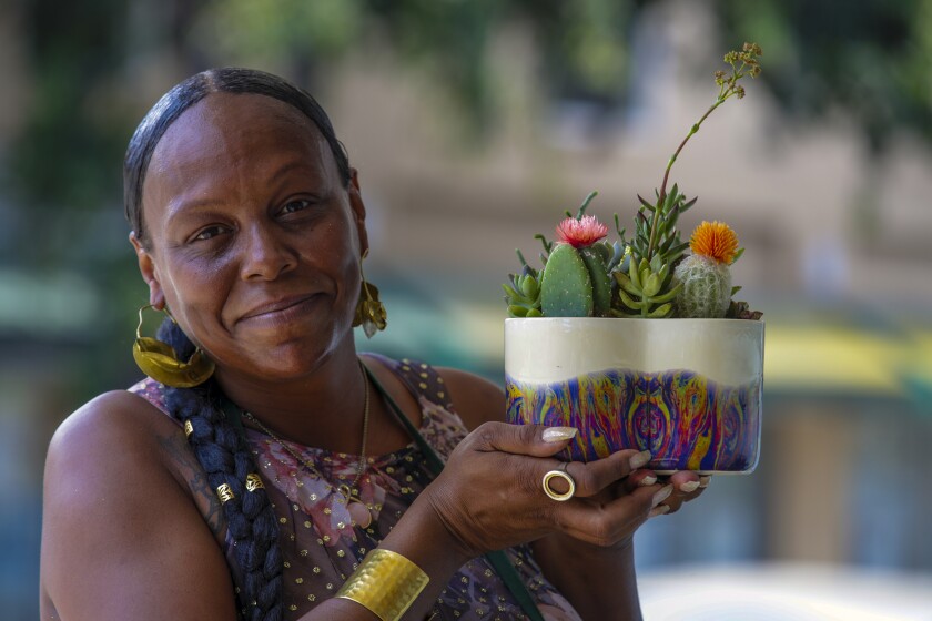 A woman with braids and large gold earrings holds a succulent arrangement in a colorful pot. 