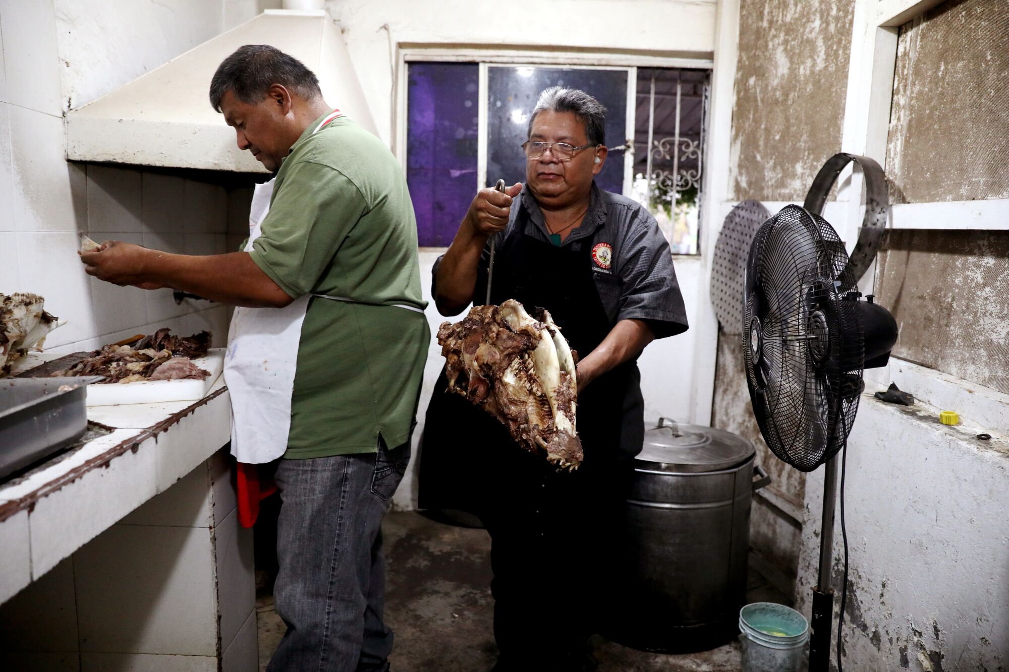 Rosendo Godinez, left, and his brother Cesar Godinez, remove the meat from cooked cows heads.