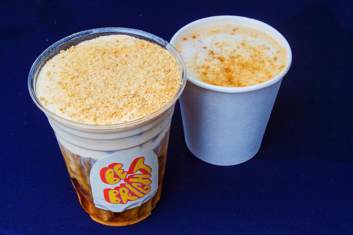 Two cups of Be Bright Coffee Pumpkin Spice Latte, one with graham cracker crumble topping.