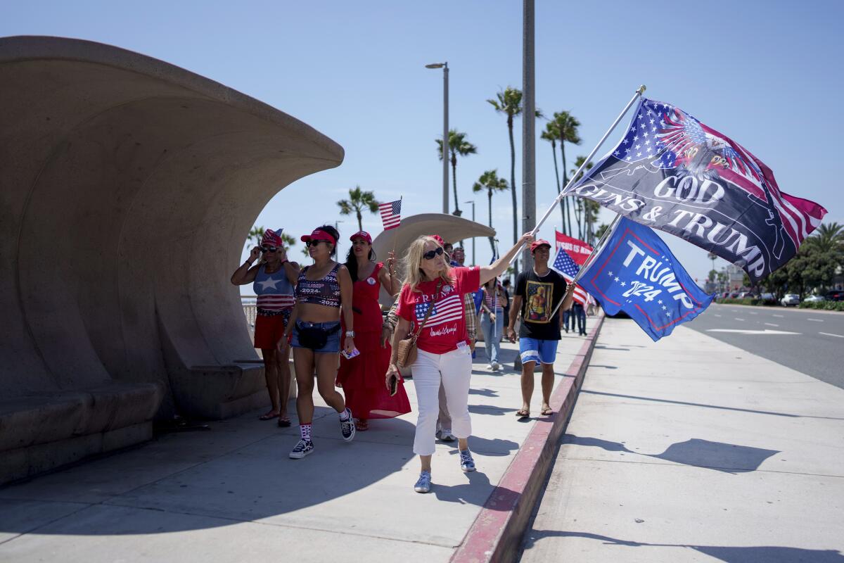 A crowd waves Trump flags, one reading "God, Guns & Trump"