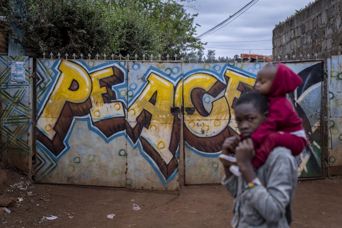 A boy carries a baby past a gate on which is written "Peace" in the Kibera neighborhood of Nairobi, Kenya Sunday, Aug. 14, 2022. Kenyans attended regular church services on Sunday, at which many pastors preached a message of patience and peace, as the country continues to wait for the results of Tuesday's presidential election. (AP Photo/Ben Curtis)