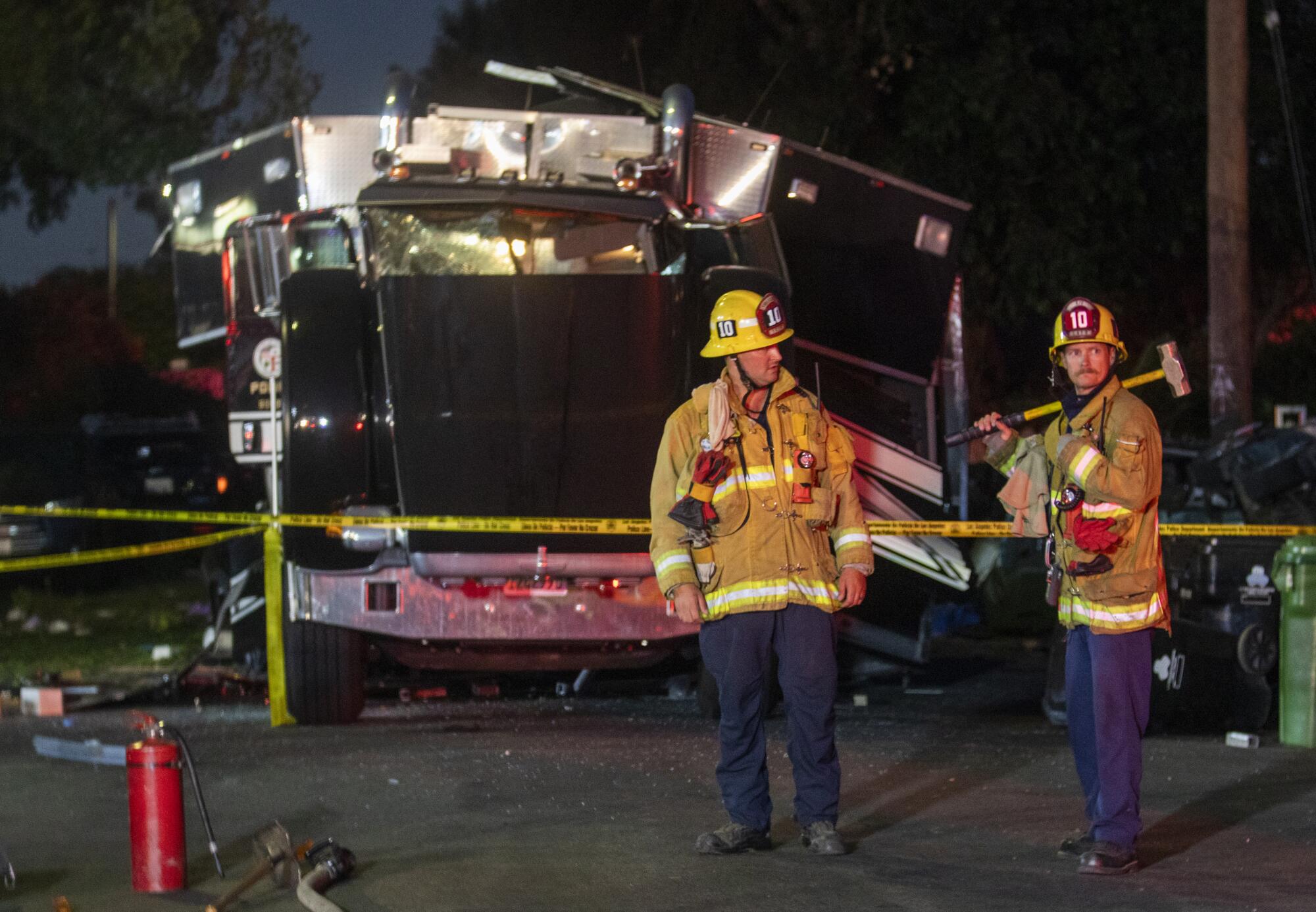 Two firefighters stand in front of damaged semitruck.