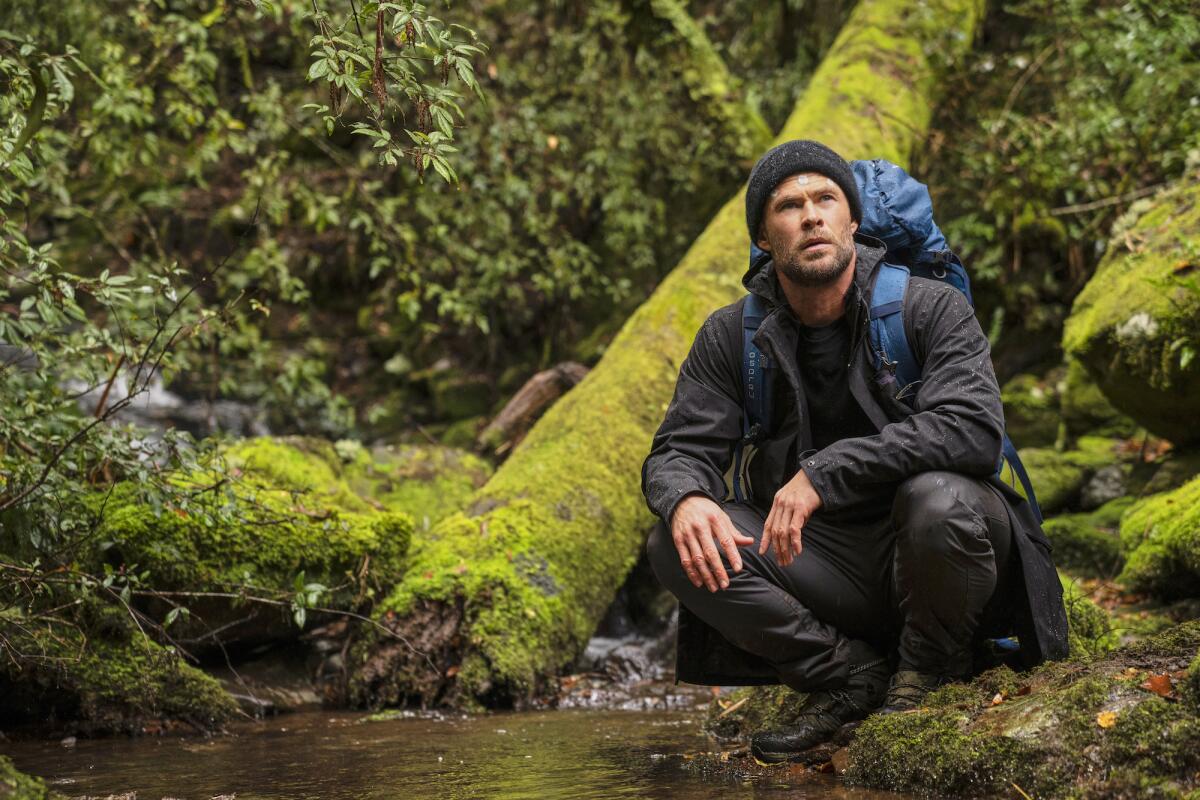 A man in hiking gear with a backpack crouches by the edge of a pond on a hike in "Limitless."