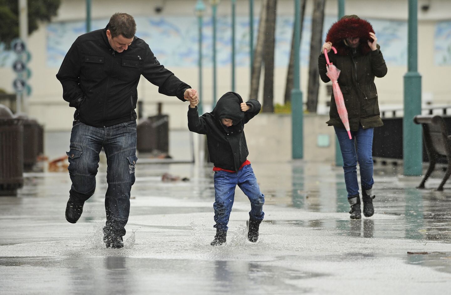 Scott Hesford-Hensler, left, plays in the rain with his son Jayden, 5, and wife Danielle, right, at King Harbour in Redondo Beach.