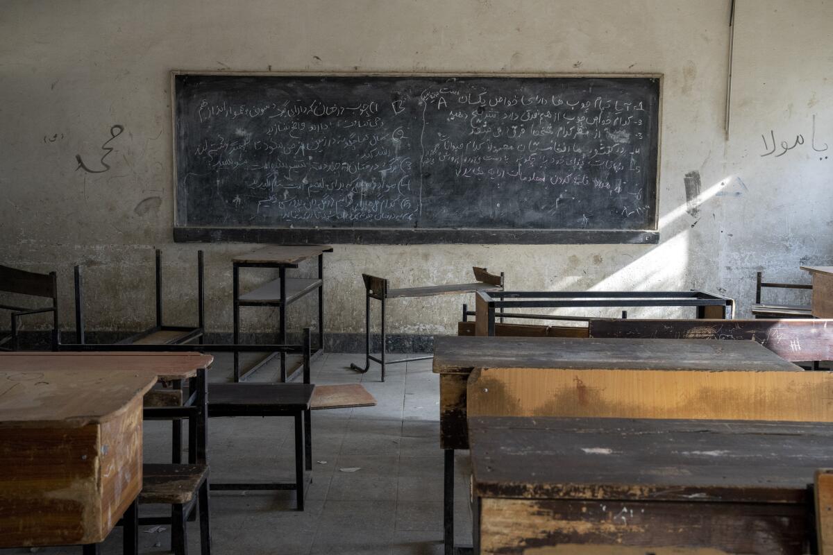 A classroom with a blackboard with writing on it sits empty.