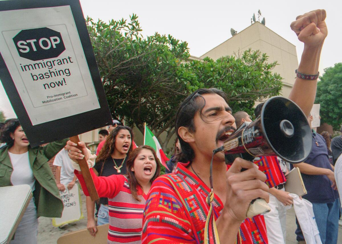 People with a bullhorn and signs rally against Proposition 187.