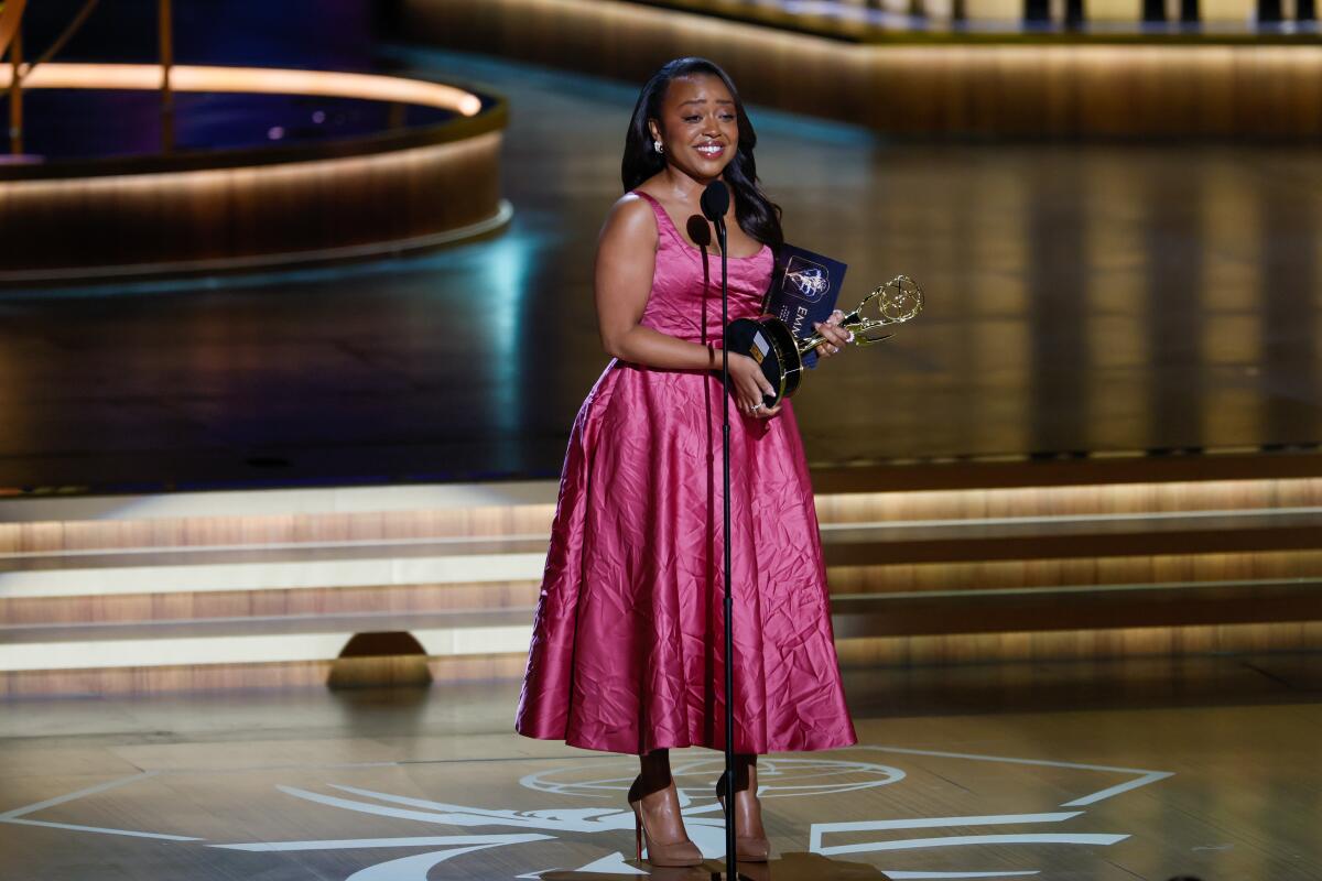 Quinta Brunson accepts her second Emmy Award while wearing a pink tea-length gown.