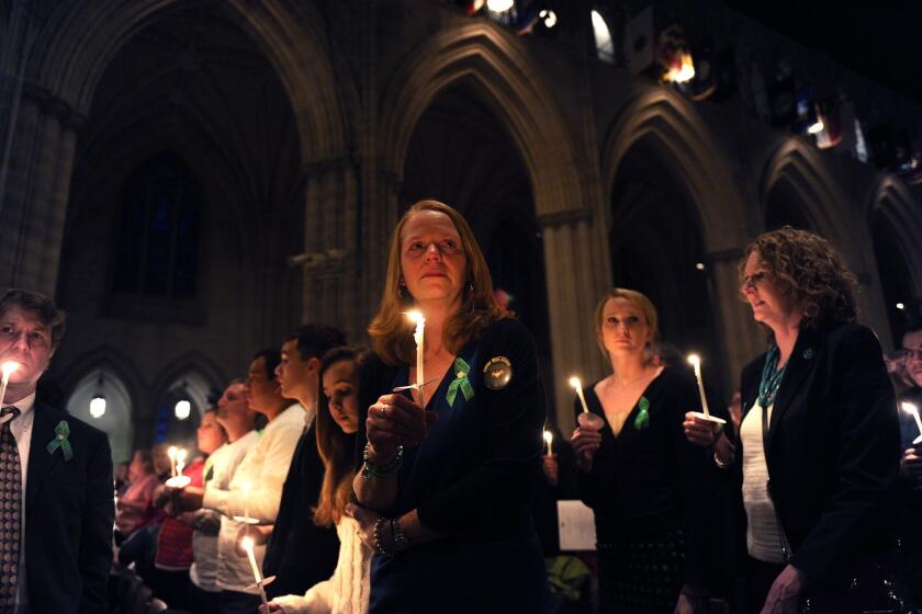 Miranda Pacchiana, center, of Newtown, Conn., holds a candle at Washington National Cathedral in Washington during a vigil for victims of gun violence. The vigil was two days before the first anniversary of the massacre at Sandy Hook Elementary School in Newtown.