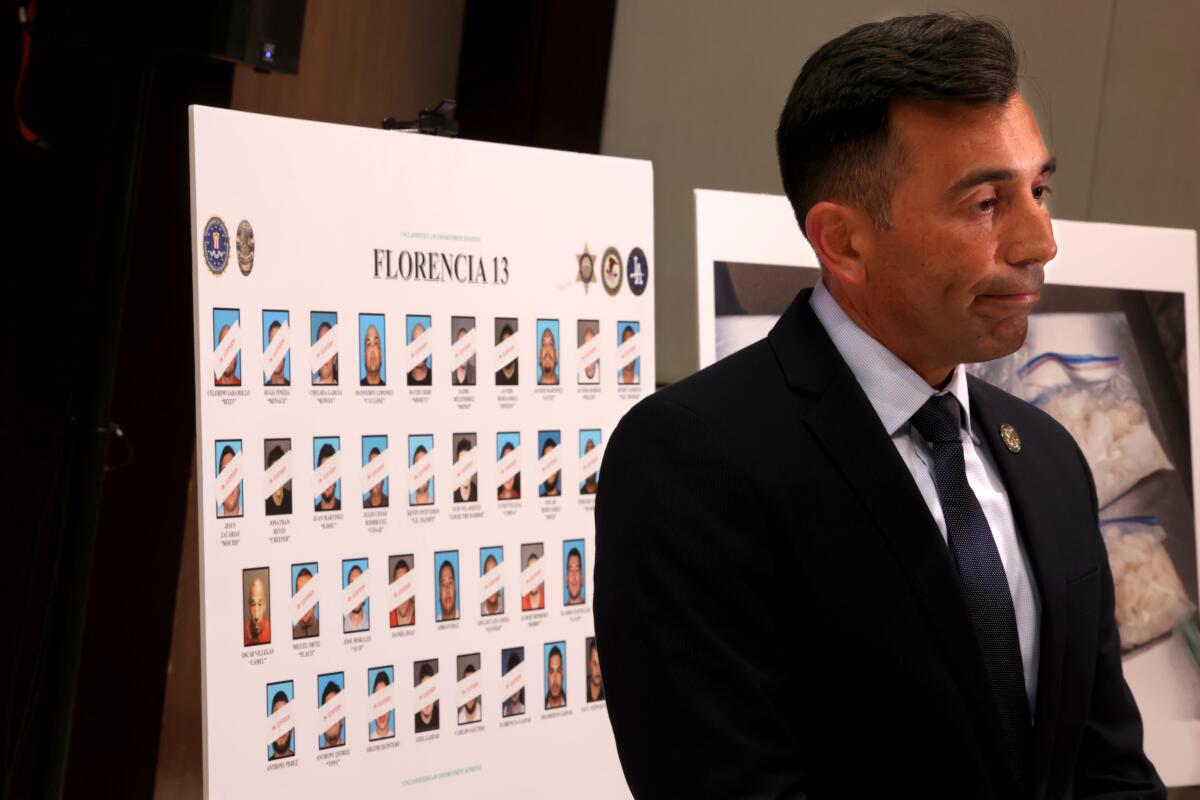 United States Attorney Martin Estrada stands next to photos on a poster