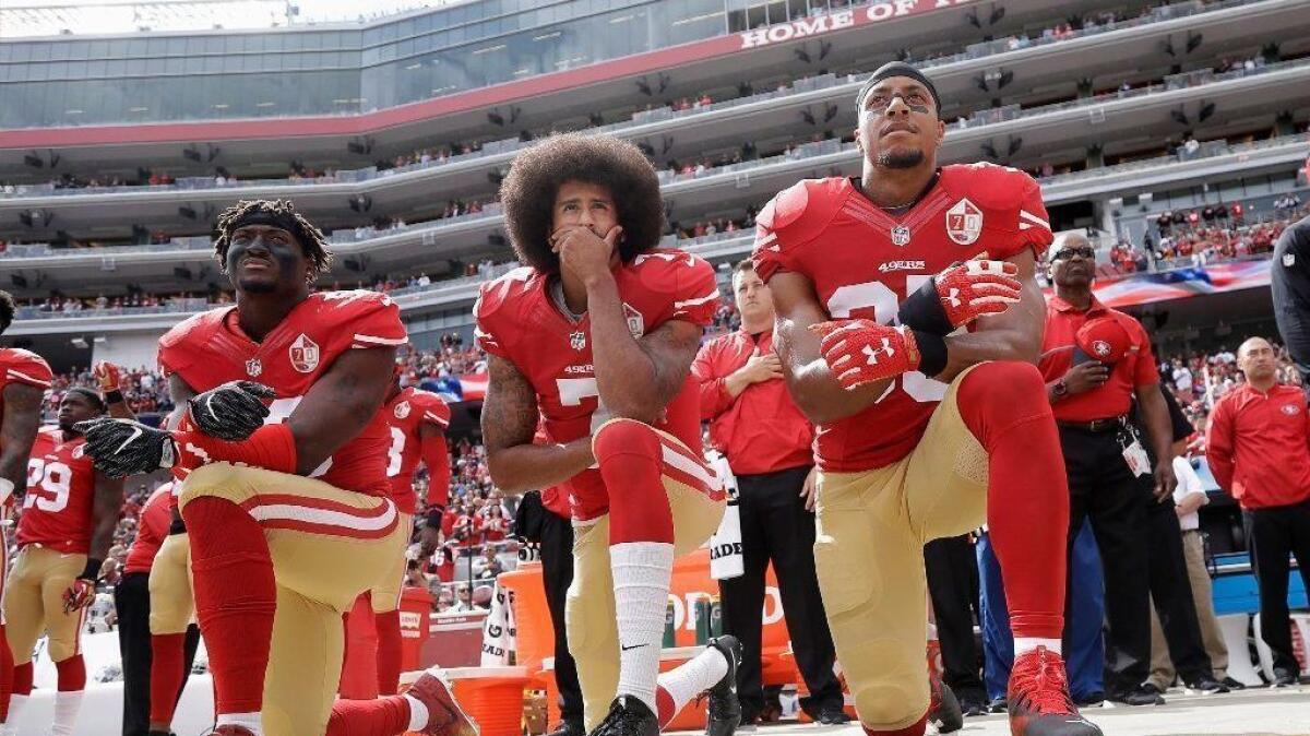 Former San Francisco 49ers quarterback Colin Kaepernick kneels before a 2016 game, flanked by teammates Eli Harold and Eric Reid, as a protest against police brutality.