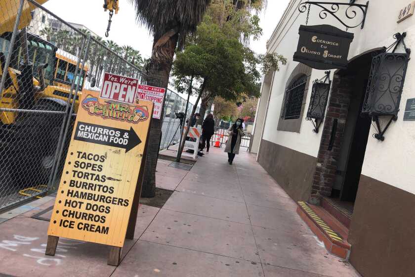 A sandwich board for Mr. Churro advertises tacos, sopes, tortas and churros in front of a security fence