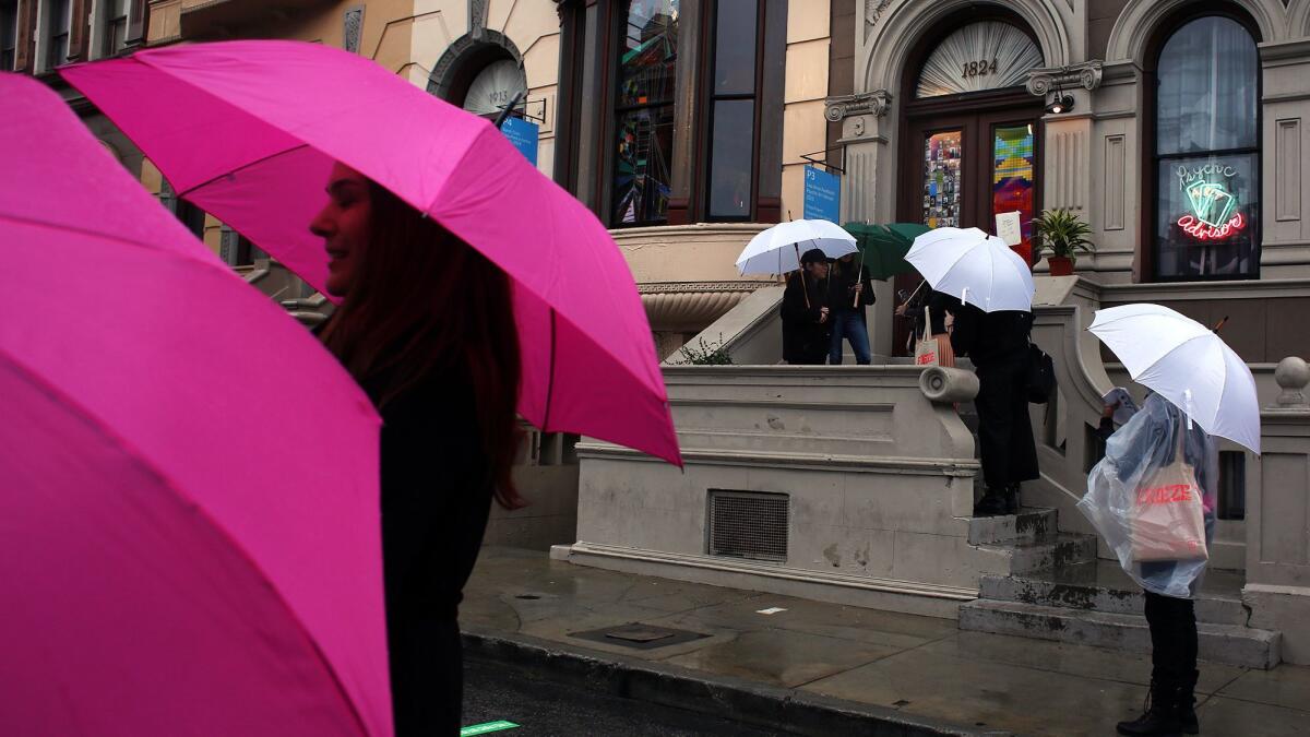 With pink Frieze umbrellas shielding them from rain on the Paramount studio back lot, people attending the art fair's Thursday preview walk past Lisa Anne Auerbach's "Psychic Art Advisor."