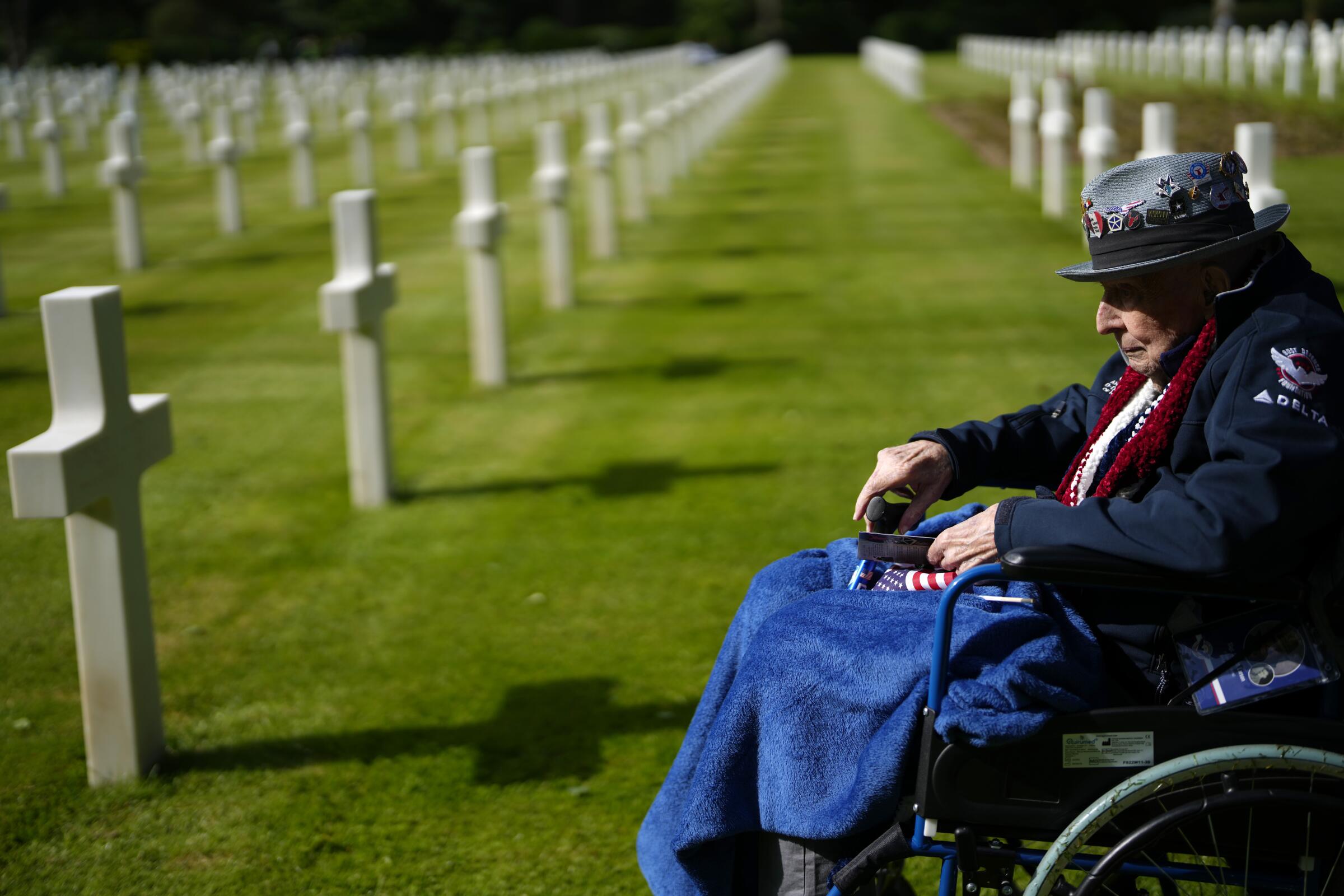 D-Day veteran Jake Larson looks at a grave while sitting in a wheelchair at a cemetery.