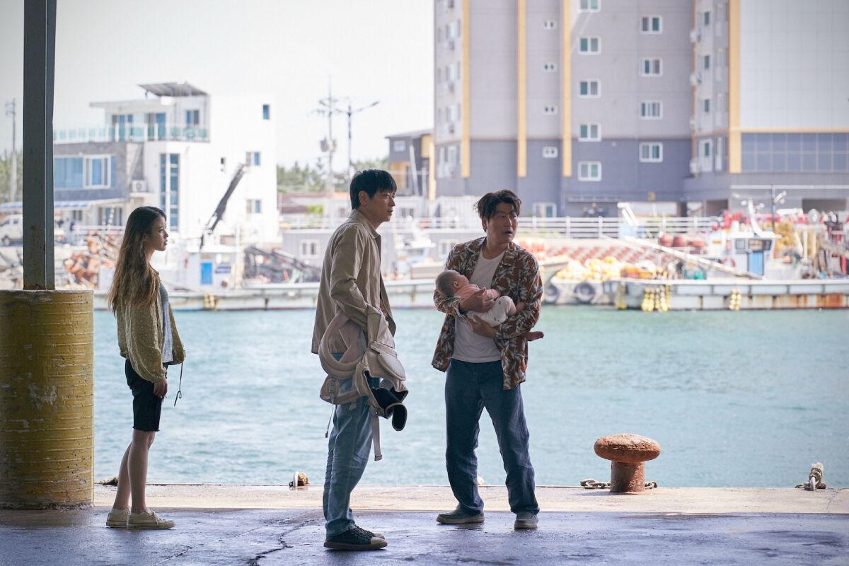 A woman, a man and another man with a baby are standing at the harbor.