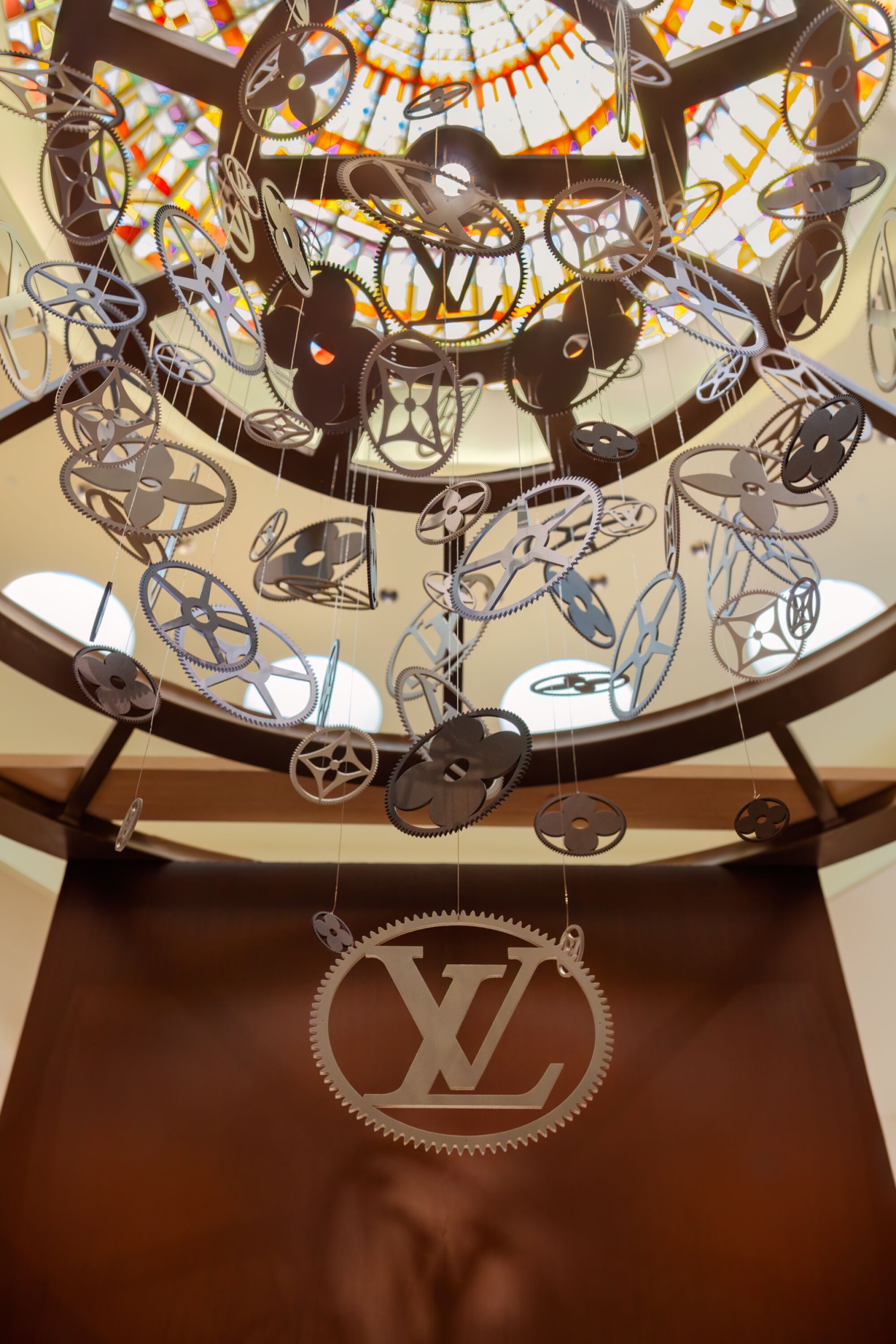 Un groupe de disques métalliques à motifs suspendus à un plafond en forme de dôme au-dessus d'une plus grande découpe métallique du logo Louis Vuitton