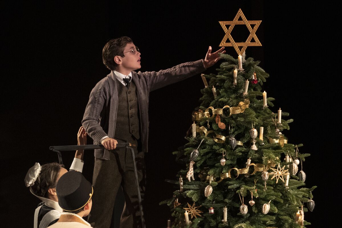 A boy places a Star of David atop a Christmas tree. 