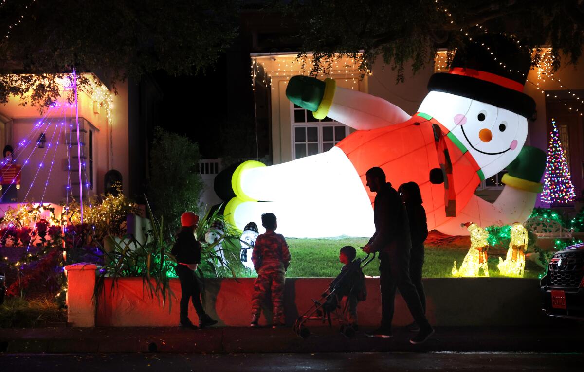 People walk by houses decked with string lights, and inflatable and homemade holiday decorations.