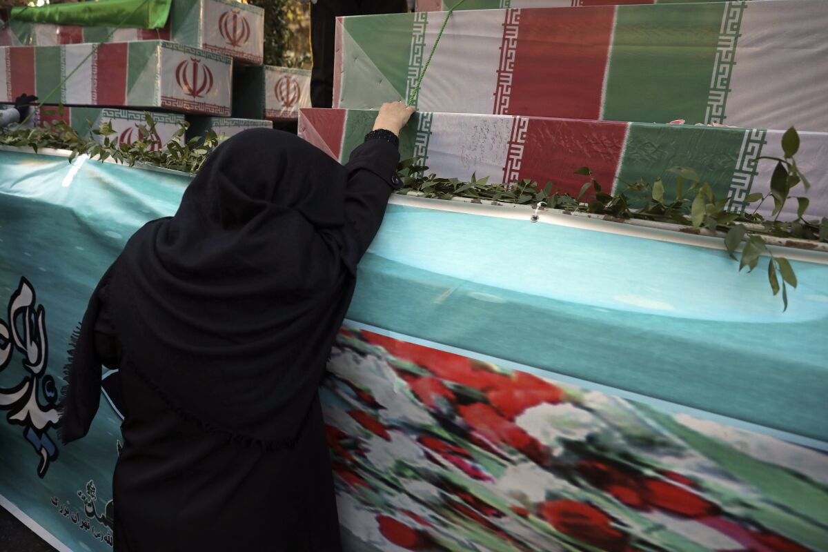 An Iranian woman mourns next to flag-draped caskets of unknown soldiers who were killed during the 1980-88 Iran-Iraq war, whose remains were recently recovered from former battlefields, during their funeral in Tehran, Iran, Thursday, Jan. 6, 2022. Thousands of mourners poured into the streets of Iranian cities on Thursday for the mass funeral of 250 victims of the war, a testament to the brutal conflict's widespread scale and enduring legacy 35 years later. (AP Photo/Vahid Salemi)