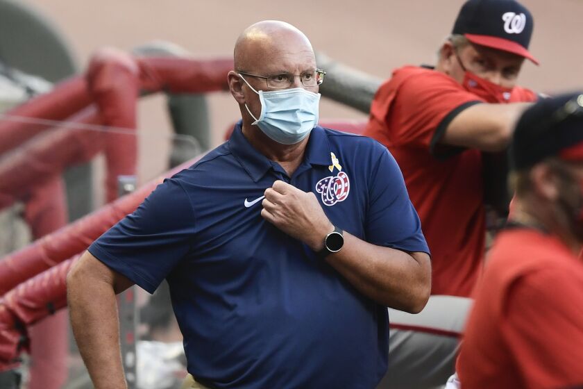 Washington Nationals general manager Mike Rizzo, left, looks on from the dugout as a baseball game.