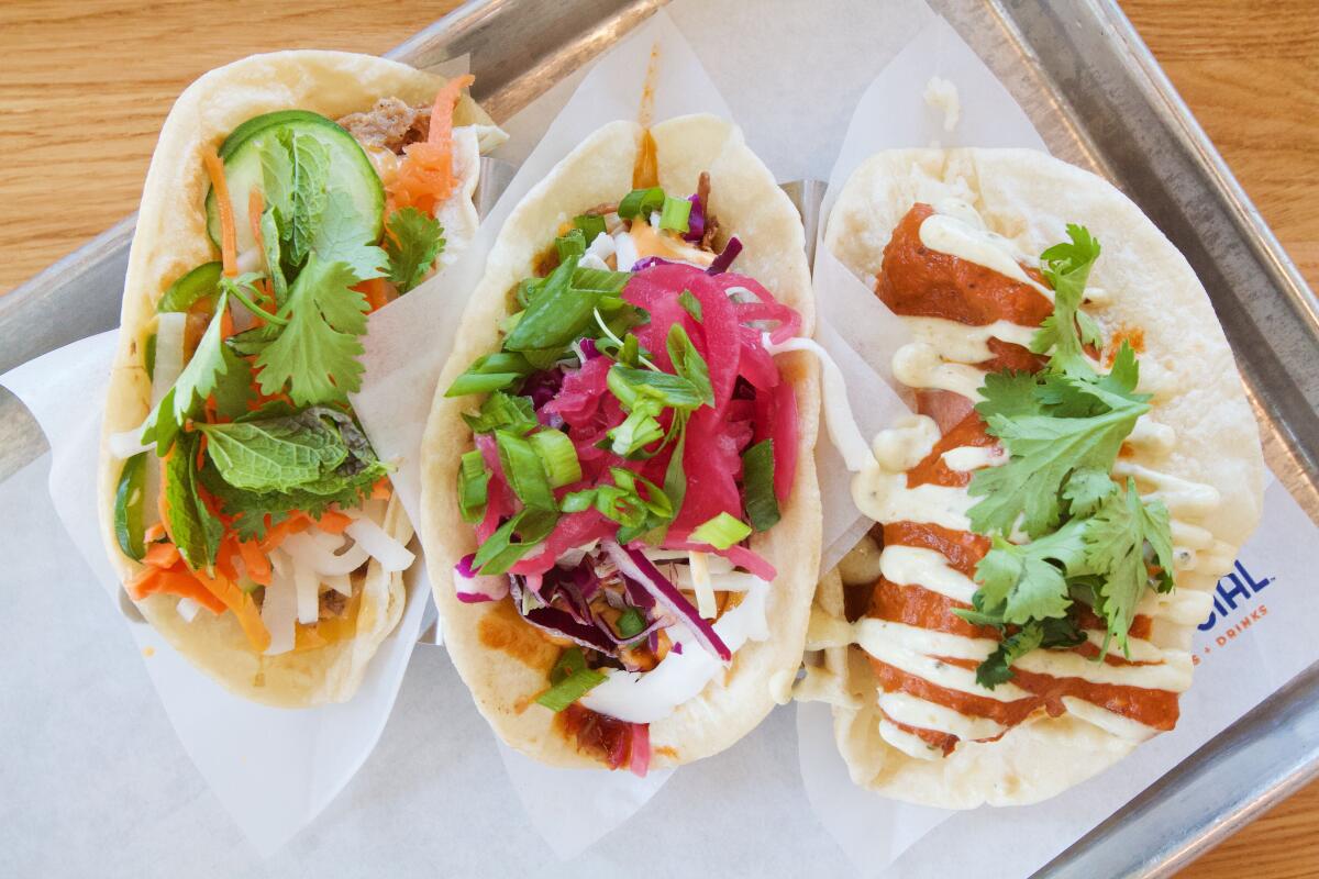 An overhead view of three tacos on paper on a silver tray