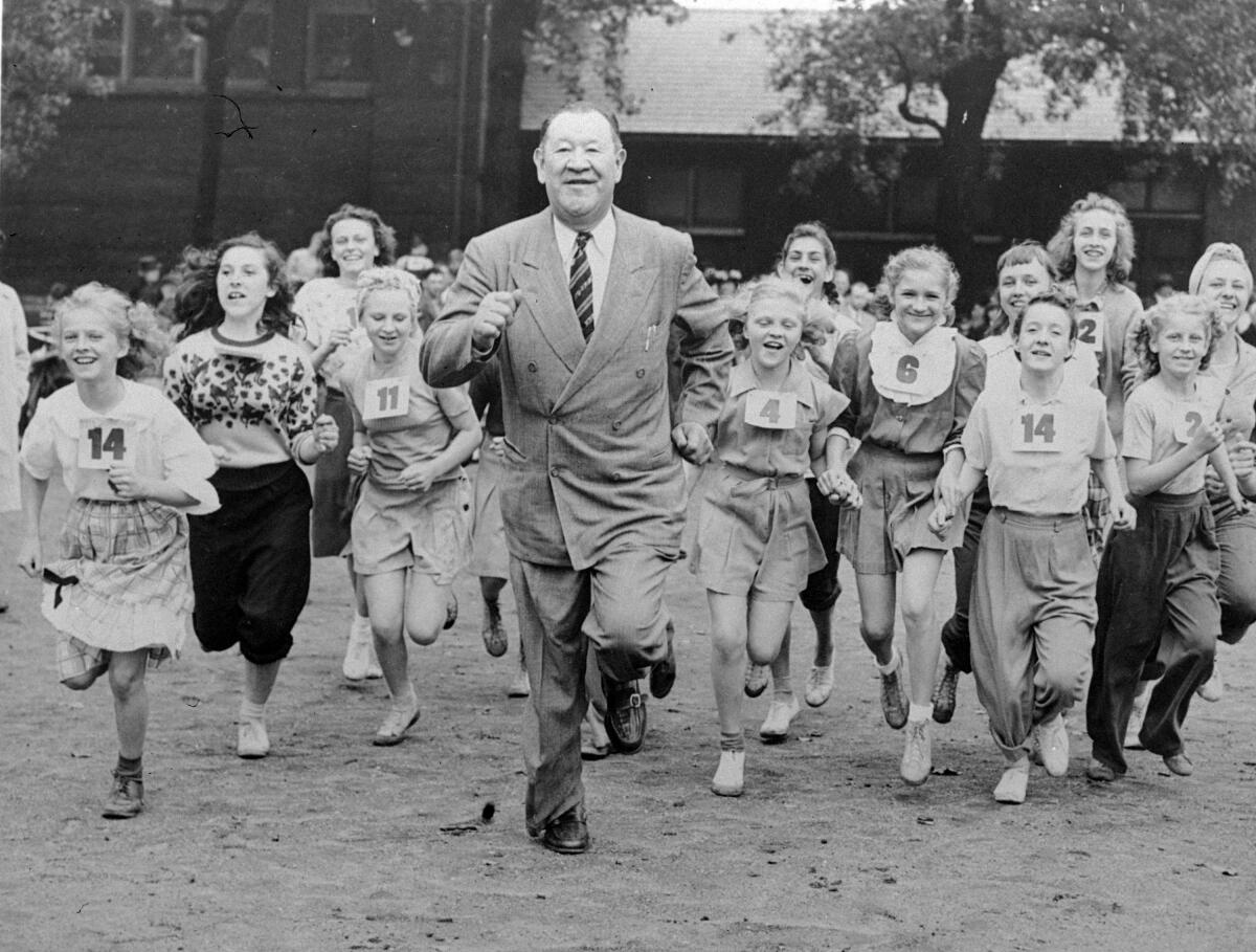 Former U.S. Olympic great Jim Thorpe running in a business sui with crowd of schoolgirls