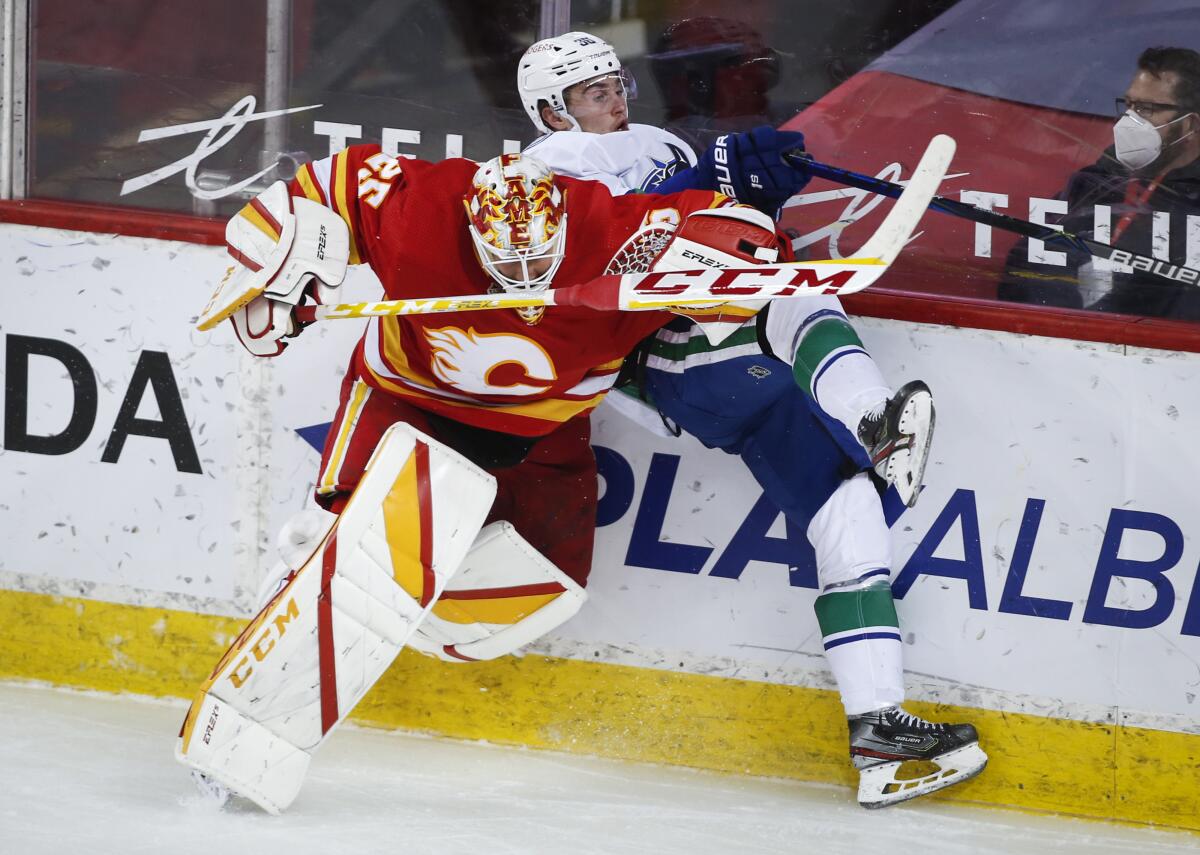 Vancouver Canucks' Nils Hoglander, right, is checked by Calgary Flames goalie Jacob Markstrom during the third period of an NHL hockey game Thursday, May 13, 2021, in Calgary, Alberta. (Jeff McIntosh/The Canadian Press via AP)