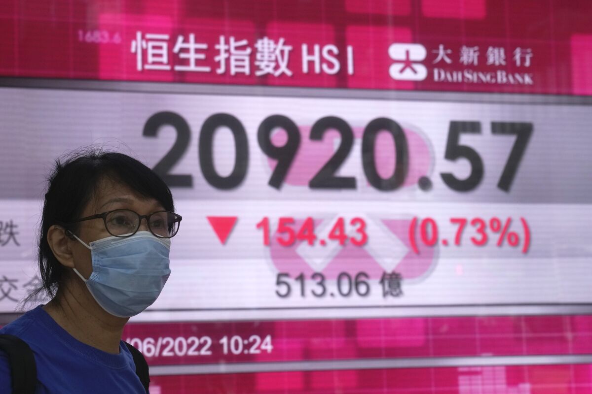 A woman wearing a face mask walks past a bank's electronic board showing the Hong Kong share index in Hong Kong, Monday, June 20, 2022. Asian markets were mostly lower in cautious trading Monday ahead of a federal holiday in the U.S. (AP Photo/Kin Cheung)