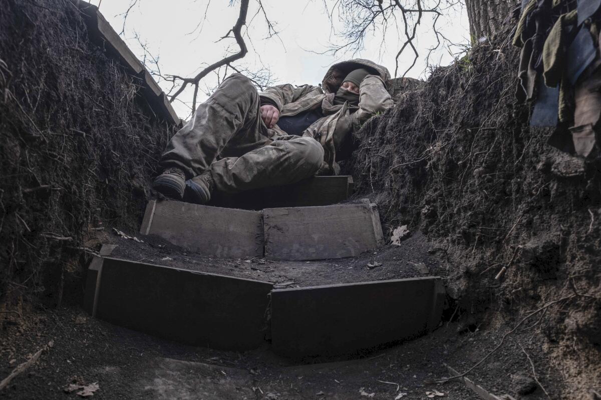 A Ukrainian soldier rests in a muddy trench.