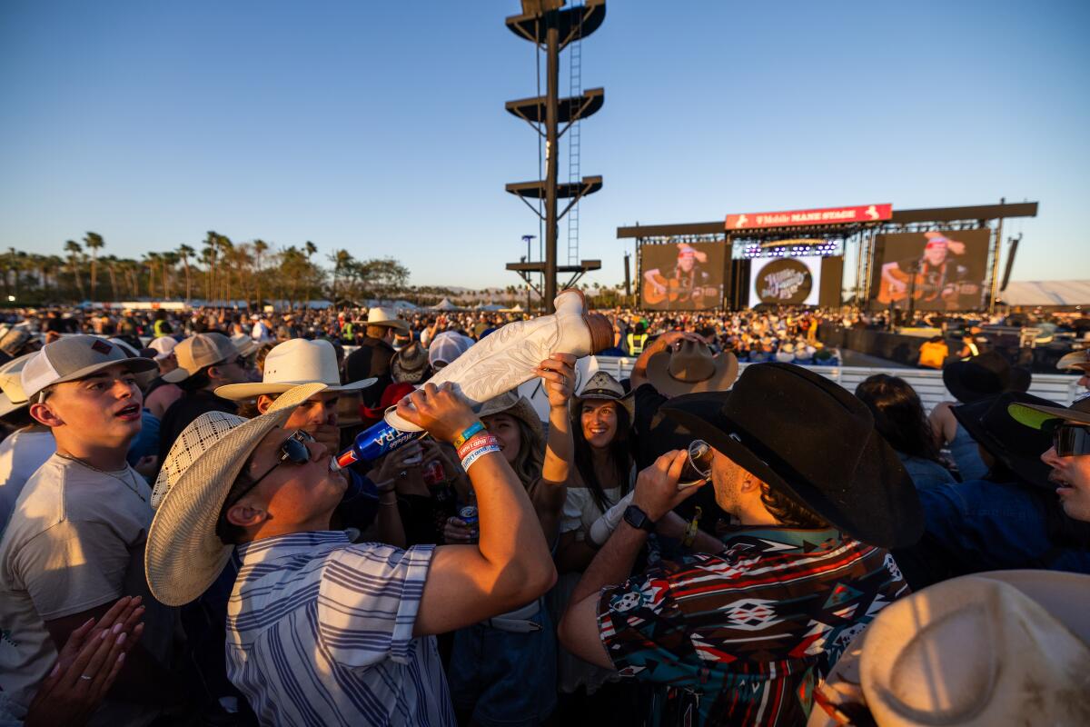 A man drinks a beer from a woman's boot while watching Willie Nelson & Family perform at the Stagecoach festival.