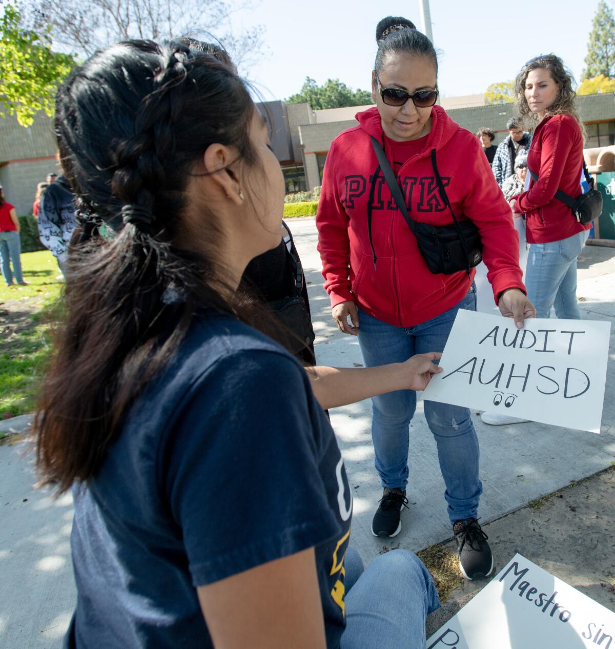 Gisele Aguilar hands a flyer protesting layoffs to Sofia Romero, a parent of students in the Anaheim district.