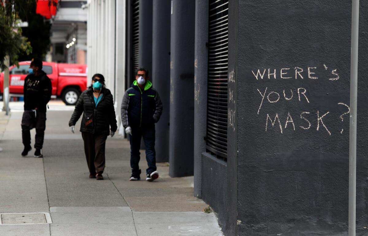 Peatones caminan frente a un graffiti que alienta el uso de máscaras, el 20 de abril de 2020, en San Francisco.