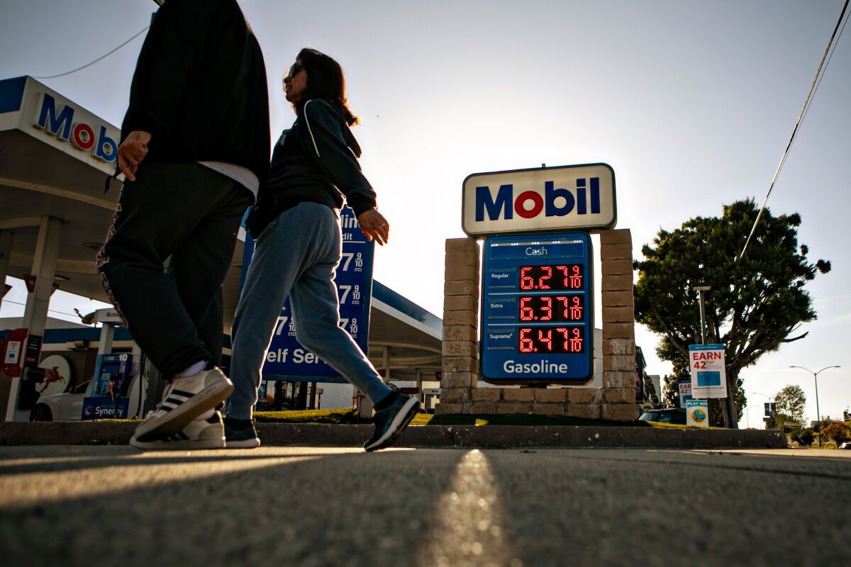 People walk by a gas station with a sign listing gas prices at $6.27 to $6.47 a gallon.