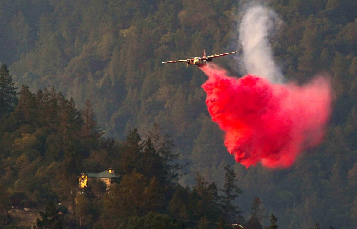 An aircraft drops a red cloud of fire retardant on tree-covered hills near California 29 in Calistoga.