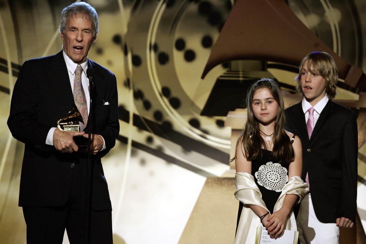 Burt Bacharach holds a Grammy statuette standing onstage with two of his children