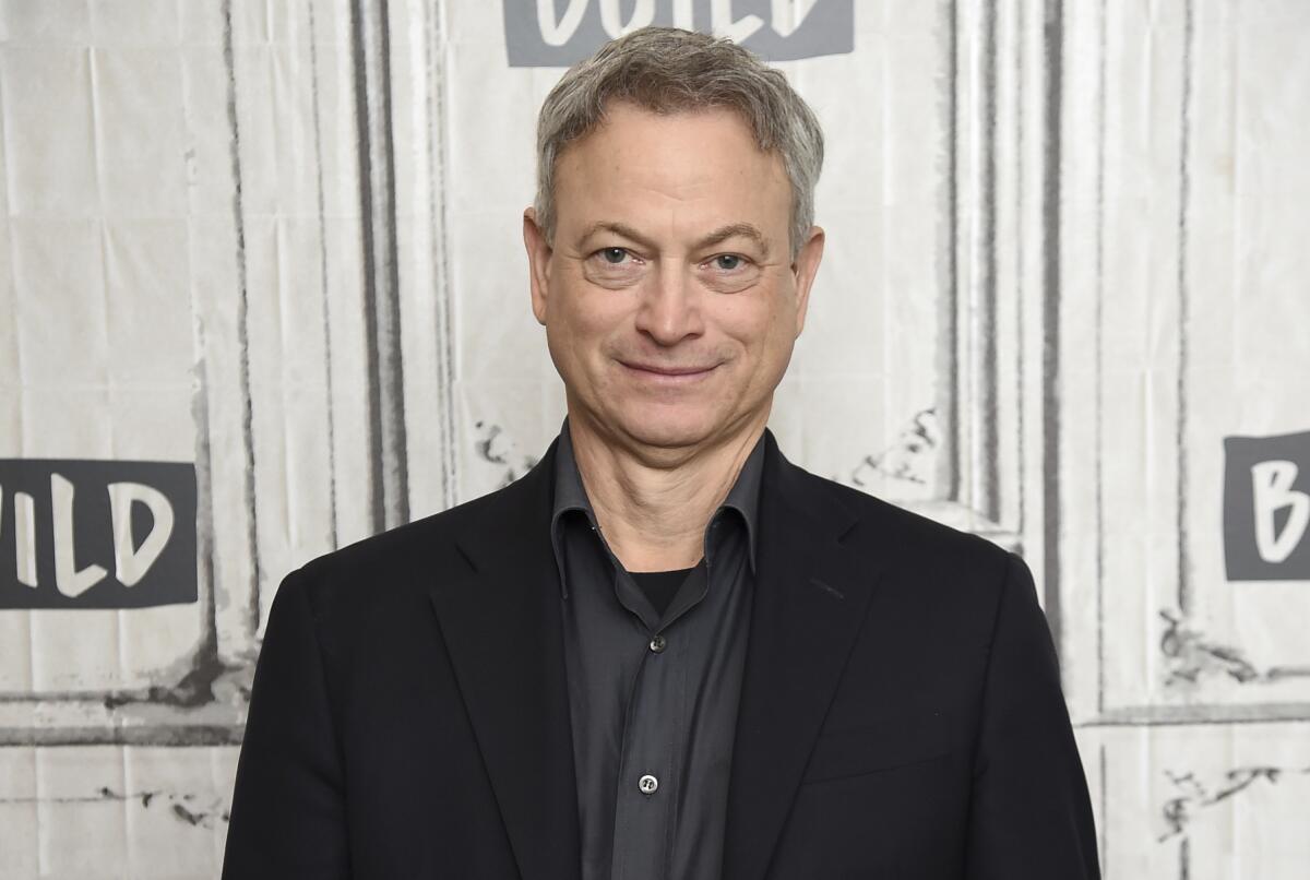 Actor Gary Sinise smiles slightly while posing at an event in a black jacket and black shirt
