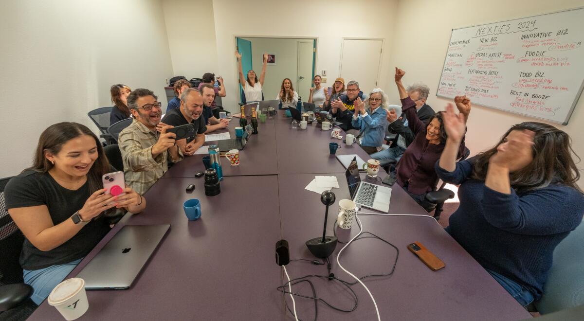 More than a dozen people sit at a conference table and raise their arms in celebration.