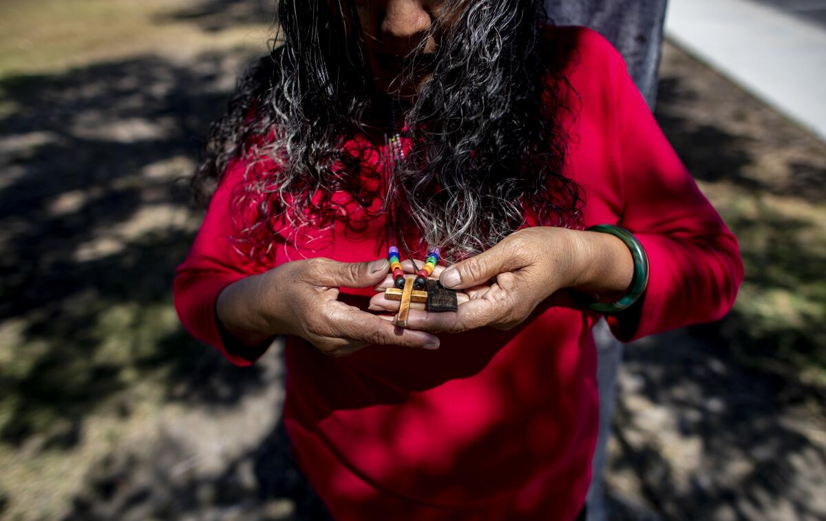 Bertha Valdez holds the cross of her keepsake necklace outside her home 