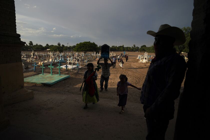 A Yaqui Indigenous family walks past the cemetery where slain water-defense leader Tomás Rojo is buried, outside a church where they arrive to celebrate the Virgin Mary in Potam, Mexico, Tuesday, Sept. 27, 2022. Mexico has become the deadliest place in the world for environmental and land defense activists, and the Yaqui Indigenous people of northern Mexico are still mourning the killing of Rojo in June 2021. (AP Photo/Fernando Llano)
