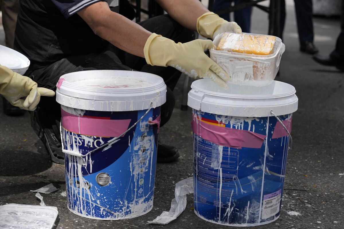 A Thai customs official shows how packages of heroin were concealed within a bucket of thick paint during a press conference at the customs headquarters in Bangkok, Thailand, Tuesday, July 6, 2021. Customs officials said they seized almost 315 kilograms (694 pounds) of heroin worth 943.89 million baht ($29.4 million ) on Monday during an inspection of goods that were to be shipped to Australia, marking Thailand's largest single heroin seizure this year and and bringing the cumulative total of the seized drug to two tons. (AP Photo/Sakchai Lalit)