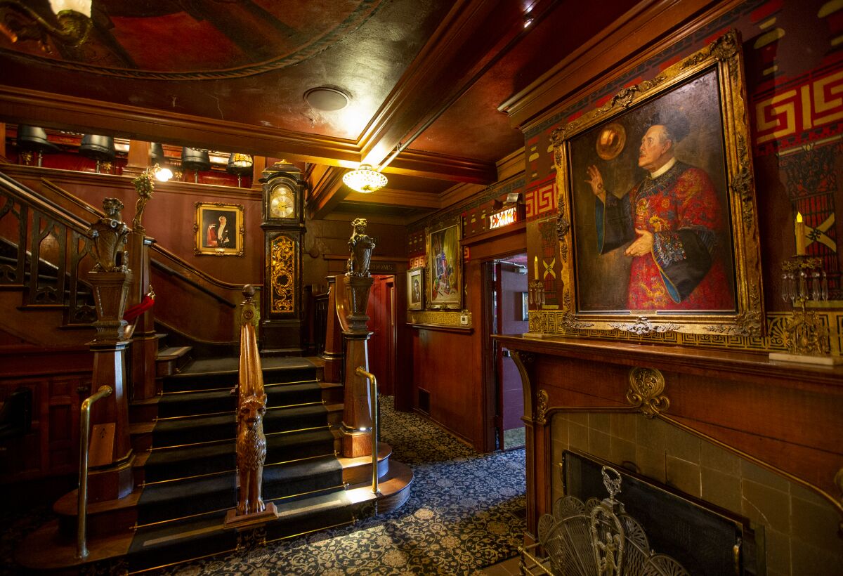A wood paneled entryway with ornate carved banisters, carpeted steps, and paintings on the walls