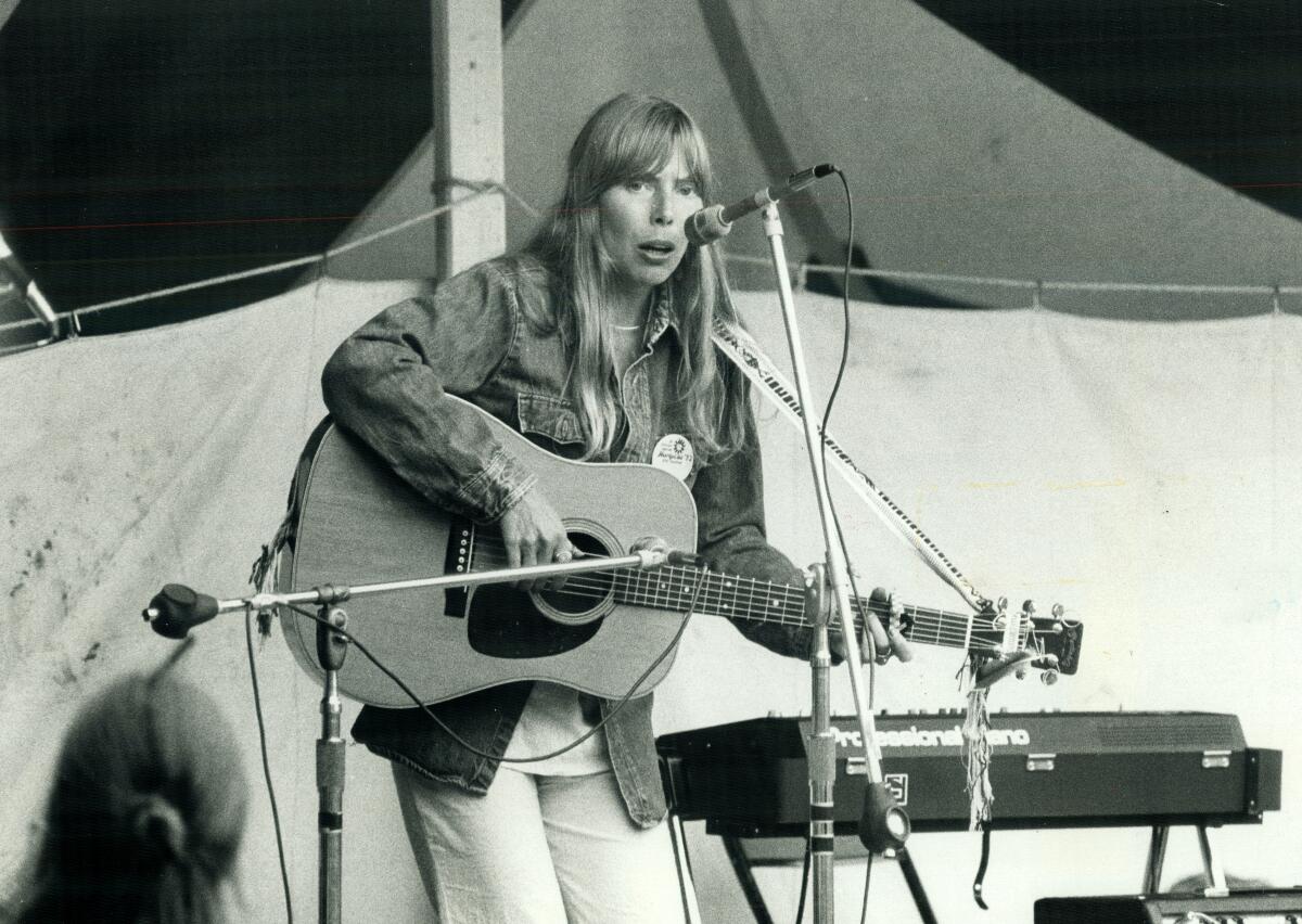 A black and white photo of a woman on a stage playing the guitar and singing into a microphone