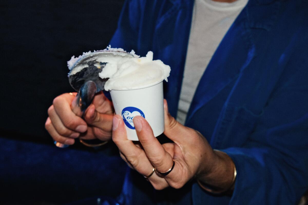 A hand scoops lemon Italian ice into a small white-and-blue paper cup by Courtney Storer's pop-up Coco's To Go-Go.