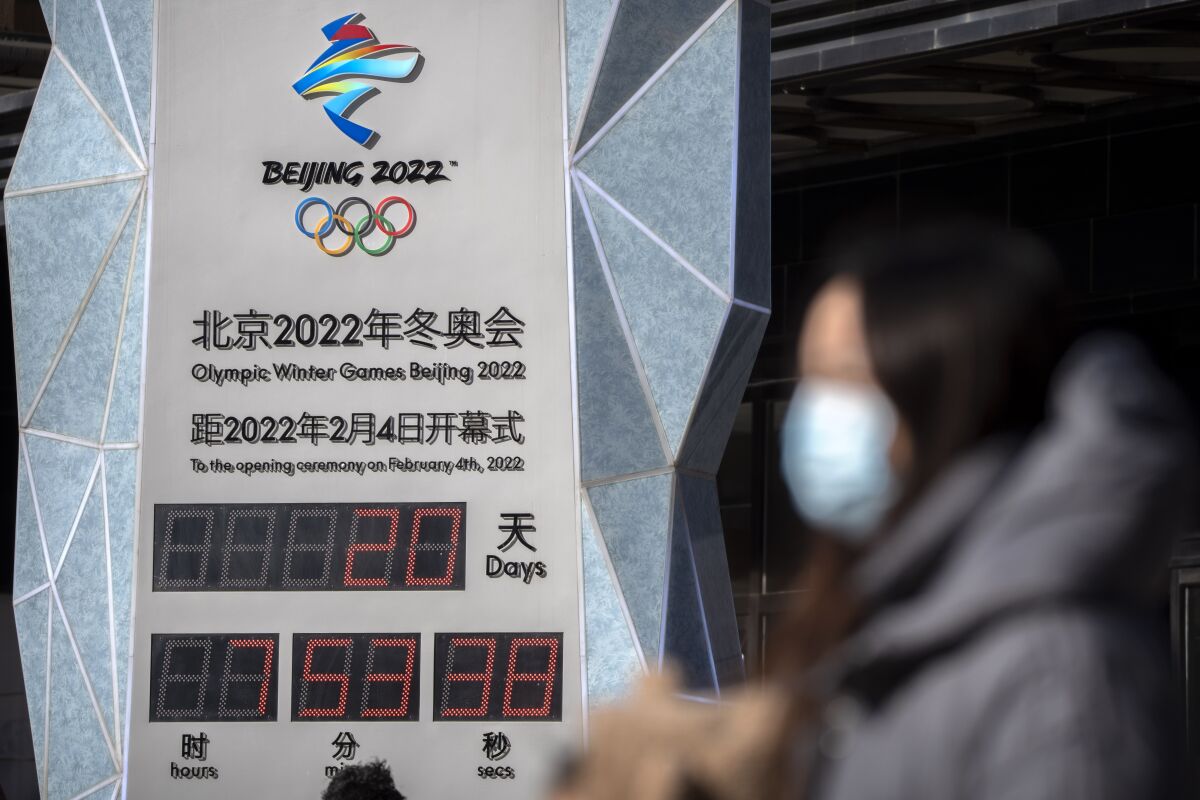 A woman wearing a face mask to protect against COVID-19 walks past a clock counting down the time until the opening ceremony of the 2022 Winter Olympics in Beijing, Saturday, Jan. 15, 2022. As the Beijing Winter Olympics loom, the Chinese capital is stepping measures to keep the coronavirus at bay including suspending most access to Tianjin, an adjacent major city which is dealing with an outbreak of the highly contagious omicron variant. These outbreaks are posing a test to its "zero-tolerance" COVID-19 policy and its ability to successfully host the Winter Olympics. (AP Photo/Mark Schiefelbein)