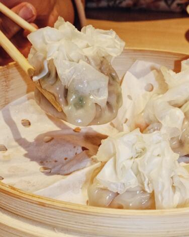 A hand holding chopsticks grabs steamed shaomai dumplings from a bamboo steam tray at Xibei Dumplings in Silver Lake.