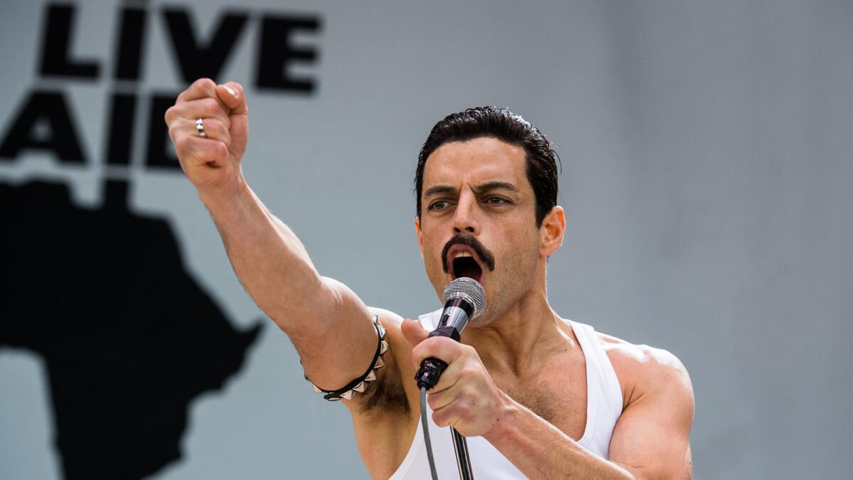 Rami Malek as Queen's Freddie Mercury holds a microphone and raises his arm in "Bohemian Rhapsody."