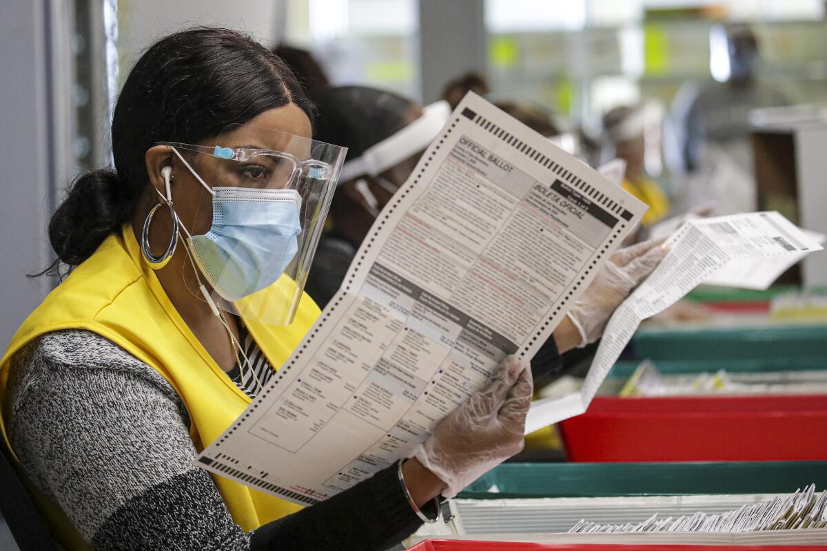 A woman in a face shield and mask looks over a printed paper ballot