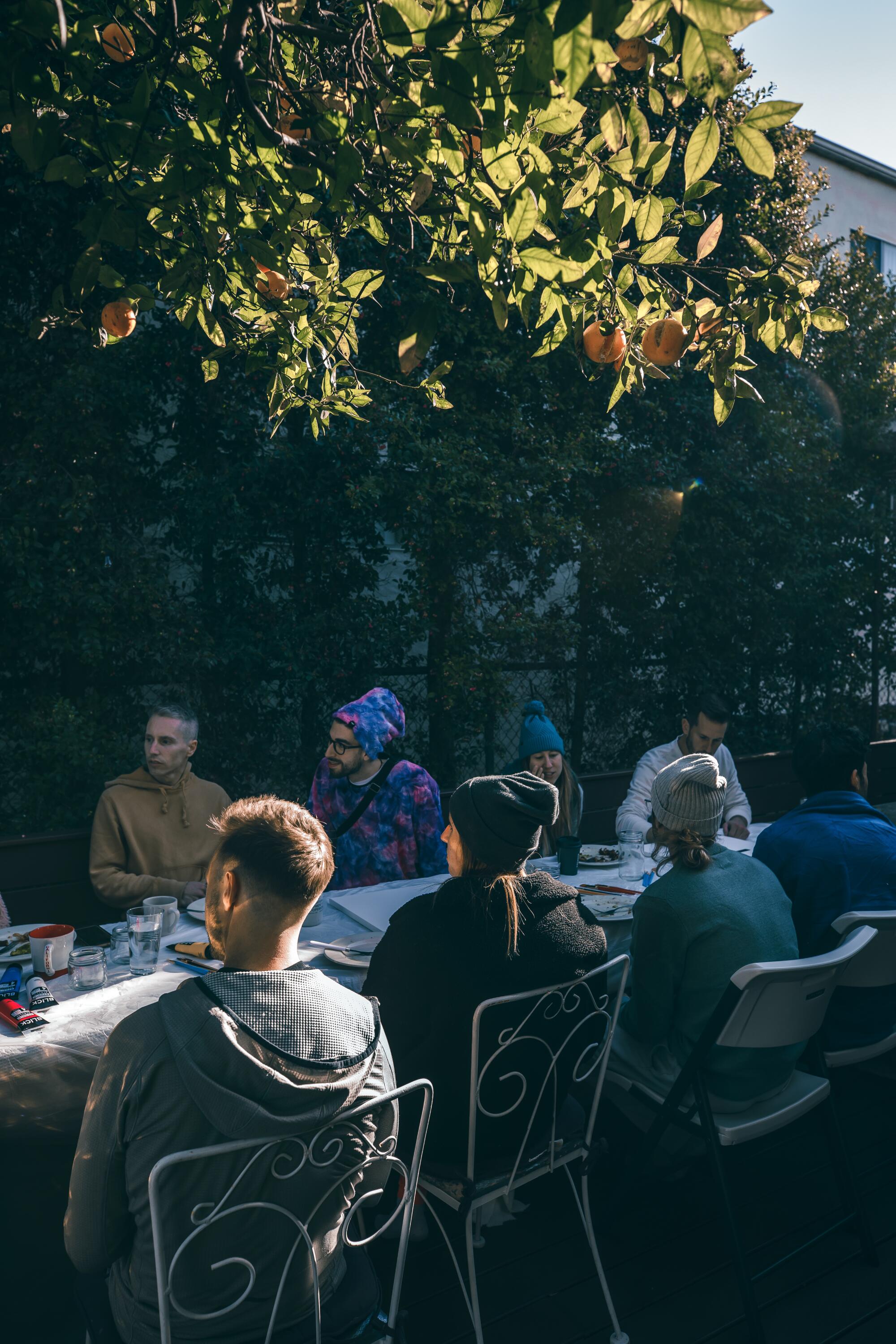 A group of people sitting in white metal chairs around a table outside.