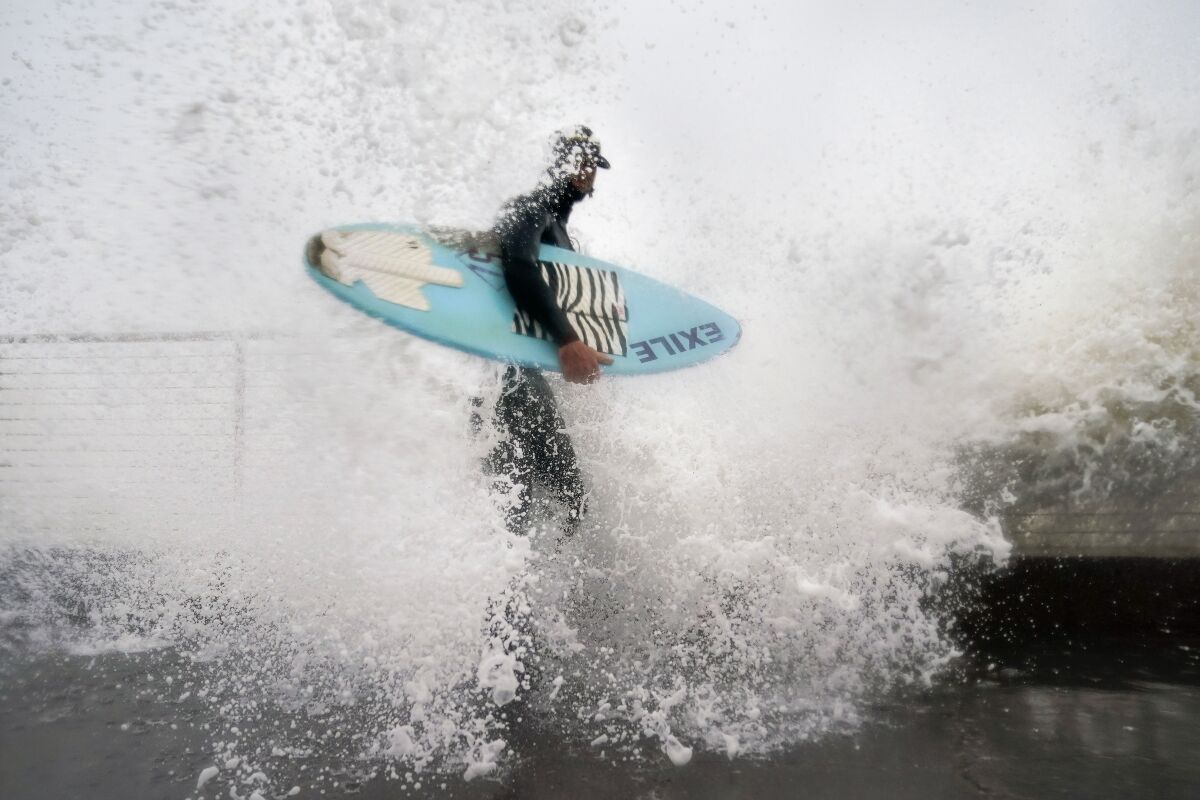 Thomas Heins is hit by a wave while standing at the seawall holding a board.